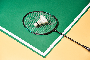 Metal badminton racket and shuttlecock on green and yellow surface with line