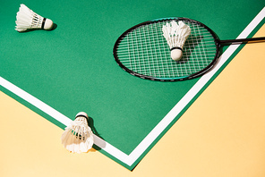 High angle view of badminton racket and shuttlecocks on green court on yellow surface