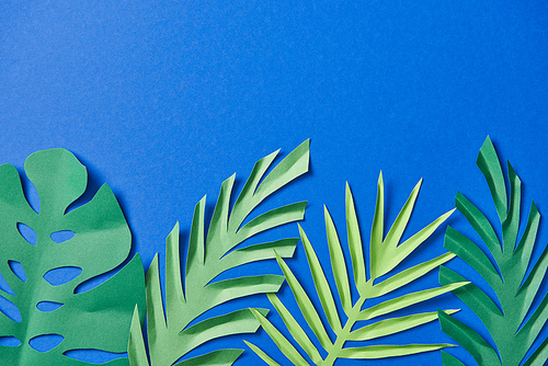 top view of green paper cut exotic leaves on blue background with copy space