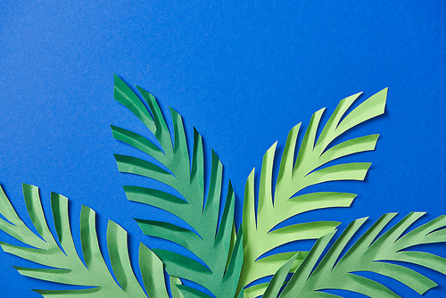 top view of green paper cut leaves on blue background with copy space