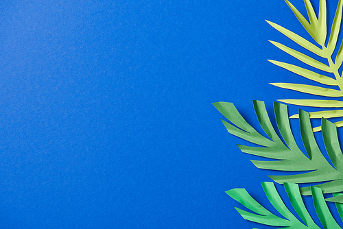 top view of green paper cut exotic leaves on blue background with copy space