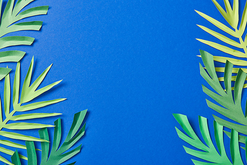 top view of green paper cut exotic leaves on blue background with copy space