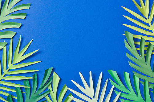 top view of green paper cut tropical leaves on blue background with copy space