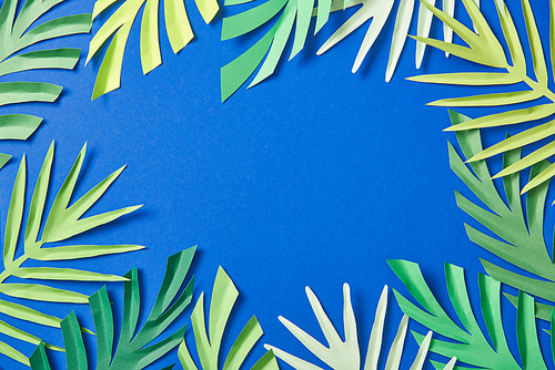 top view of green paper cut tropical leaves on blue background with copy space