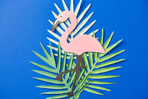 top view of green paper cut exotic leaves and flamingo on blue background