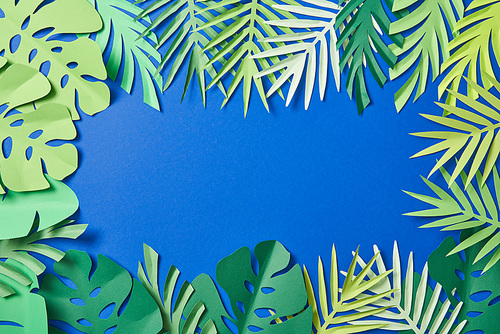 top view of green paper exotic leaves on blue background with copy space