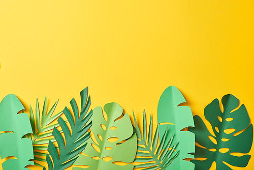 top view of paper cut green palm leaves on yellow background with copy space
