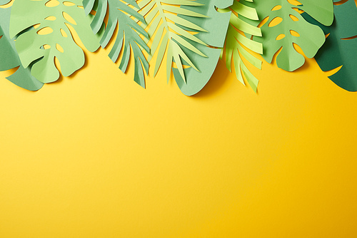 top view of paper cut green palm leaves on yellow background with copy space