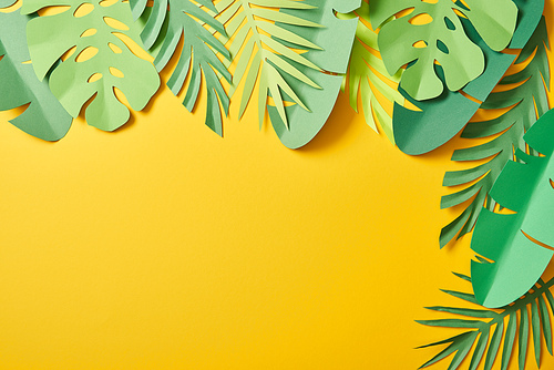 top view of paper cut green palm leaves on yellow background with copy space