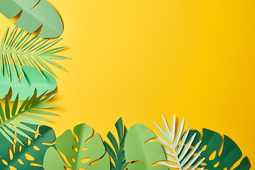 top view of paper cut green palm leaves on yellow background with copy space