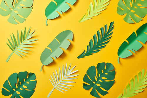 top view of paper cut green palm leaves on yellow background, seamless pattern