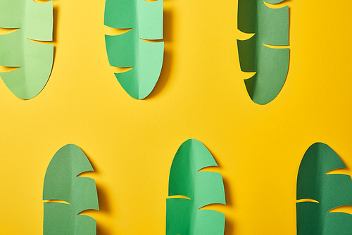 top view of paper cut green palm leaves on yellow background