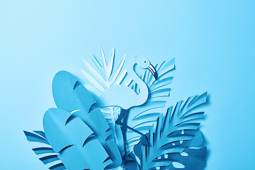 top view of blue minimalistic paper cut flamingo on palm leaves on blue background with copy space