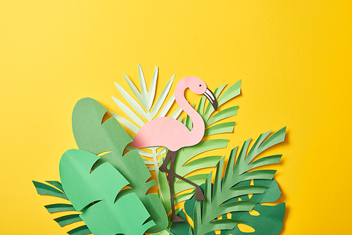 top view of paper cut green palm leaves and pink flamingo on yellow background with copy space