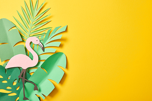 top view of paper cut green palm leaves and flamingo on yellow background with copy space