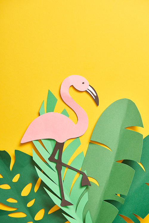 top view of paper cut green palm leaves and cute flamingo on yellow background