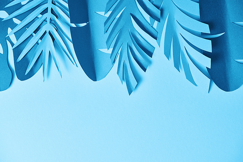 top view of blue minimalistic paper cut palm leaves on blue background with copy space