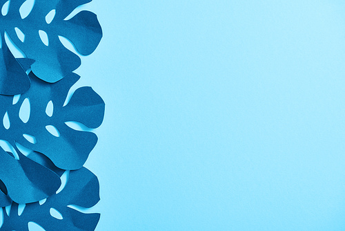 top view of blue paper cut palm leaves on blue background with copy space