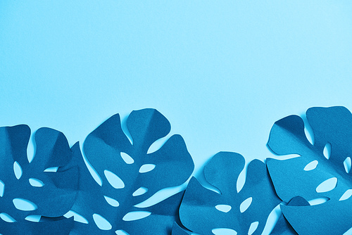 top view of blue minimalistic paper cut palm leaves on blue background with copy space