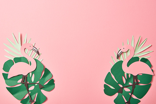 top view of paper cut flamingos on green palm leaves on pink background with copy space