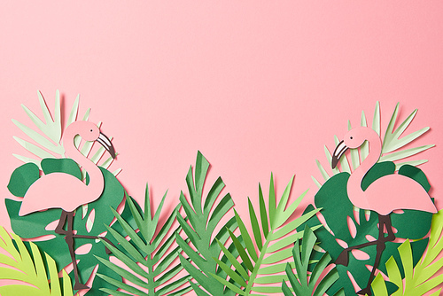 top view of paper cut flamingos on green palm leaves on pink background with copy space