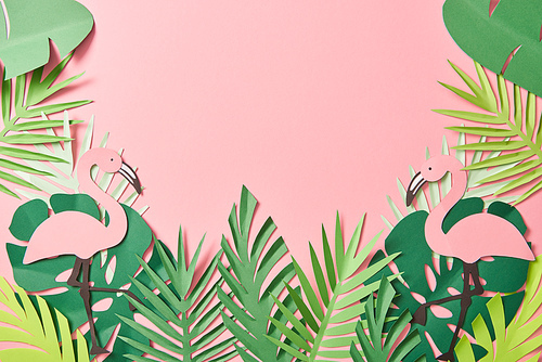 top view of paper cut flamingos on green palm leaves on pink background with copy space