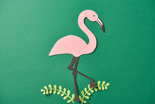 top view of paper cut leaves and pink flamingo on green background