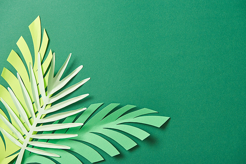 top view of exotic paper cut palm leaves on green background with copy space