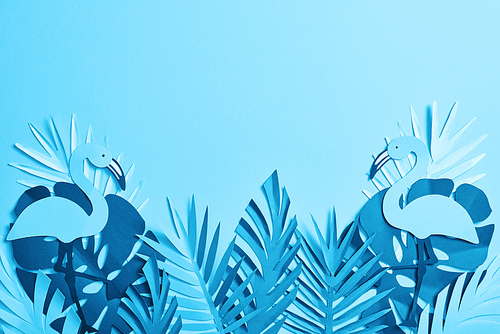 top view of blue paper cut palm leaves and flamingos on blue background with copy space
