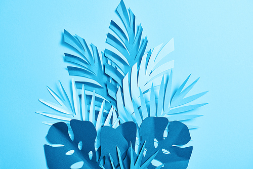 top view of blue exotic paper cut palm leaves on blue background with copy space