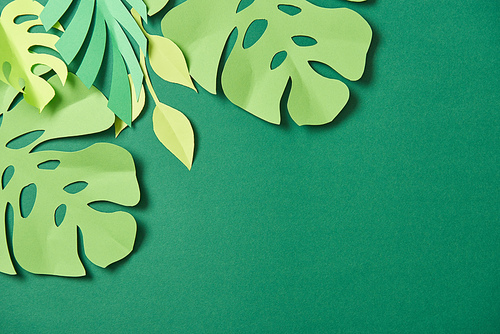 top view of exotic paper cut palm leaves on green background with copy space