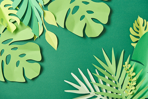 top view of exotic paper cut palm leaves on green background with copy space