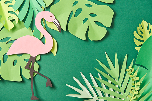 top view of exotic paper cut palm leaves and pink flamingo on green background with copy space