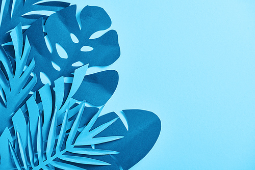 top view of blue exotic paper cut palm leaves on blue background with copy space