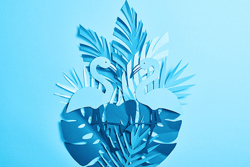top view of blue exotic paper cut flamingos and palm leaves on blue background with copy space