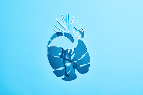top view of blue exotic paper cut palm leaves and flamingo on blue background with copy space