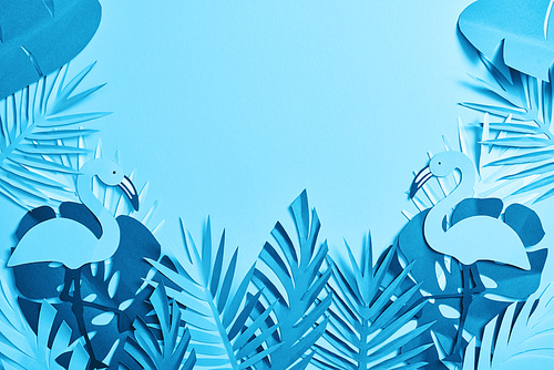 top view of blue exotic paper cut palm leaves and flamingos on blue background with copy space