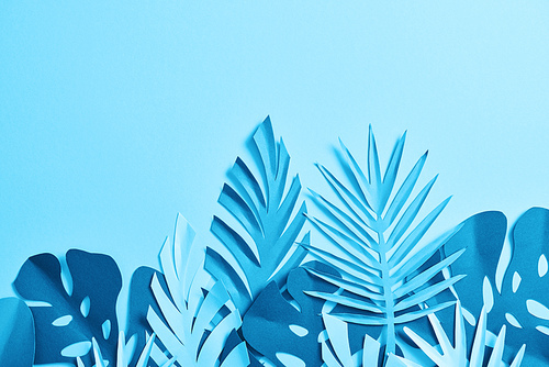 top view of blue exotic paper cut palm leaves on blue background with copy space