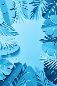 top view of blue exotic paper cut palm leaves on blue background with copy space