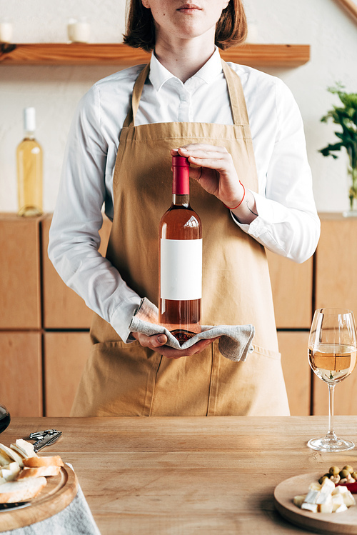 partial view of sommelier in apron holding bottle of wine