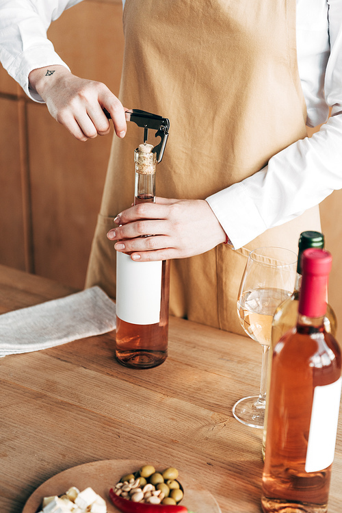partial view of sommelier in apron opening bottle of wine