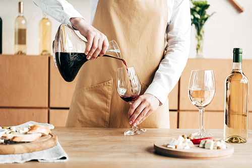 partial view of sommelier in apron holding jug and pouring wine in wine glass