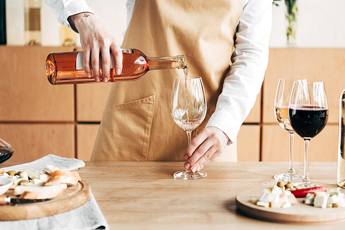 partial view of sommelier in apron holding bottle and pouring wine in wine glass