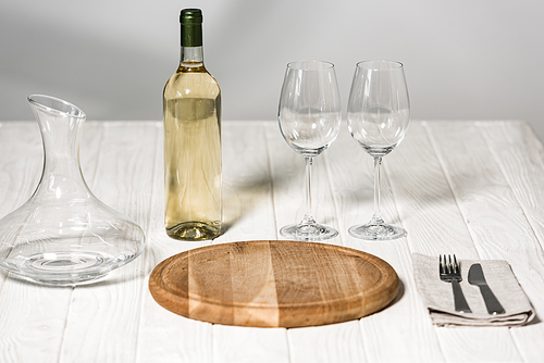 bottle of wine, jug, wine glasses, cutlery and cutting board on wooden surface in restaurant