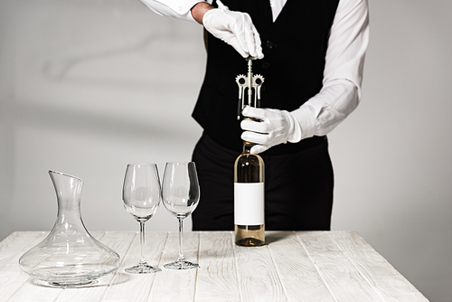 partial view of waiter in white gloves opening bottle of wine with corkscrew