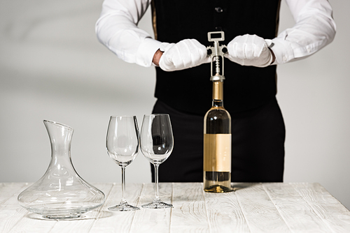 partial view of waiter in white gloves opening bottle of wine with corkscrew
