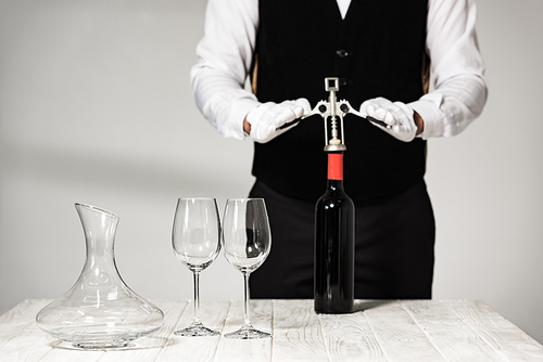 partial view of waiter in white gloves opening bottle of wine with corkscrew in restaurant