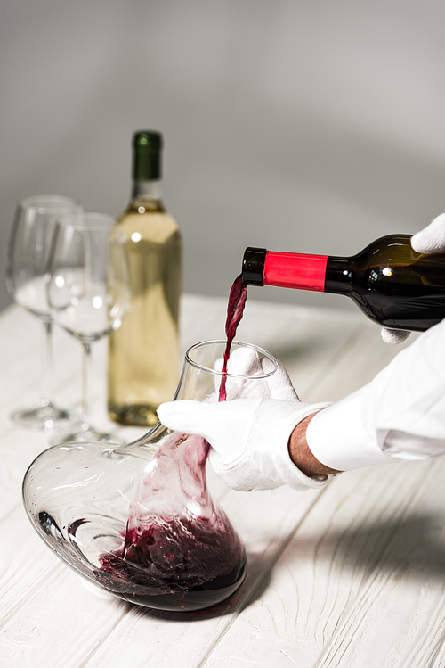 partial view of waiter in white gloves pouring wine in jug