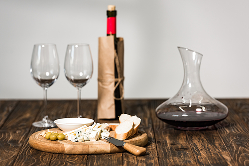 bottle of wine, wine glasses, jug, cheese, olives and bread on wooden surface