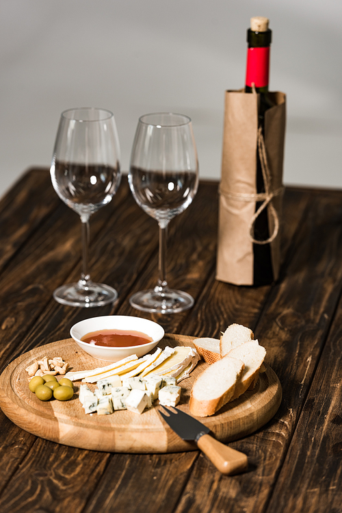 bottle of wine, wine glasses, cheese, olives, sauce and bread on wooden surface